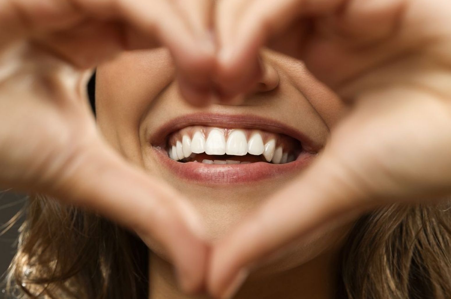 Mujer sonriendo y haciendo un corazón con la mano frente a su boca, símbolo de una sonrisa sana tras tratar la sensibilidad dental en Carrero & Tezza.
